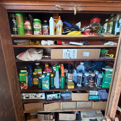 Sale Photo Thumbnail #234: Wooden garage or workshop cabinet filled with various lawn care products, chemical bottles, hardware boxes, and small electronic devices.