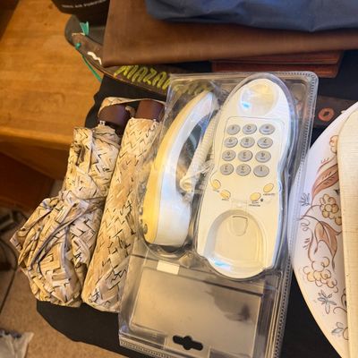 Sale Photo Thumbnail #309: Vintage white wall-mountable corded telephone in original plastic blister packaging alongside a patterned folding umbrella.
