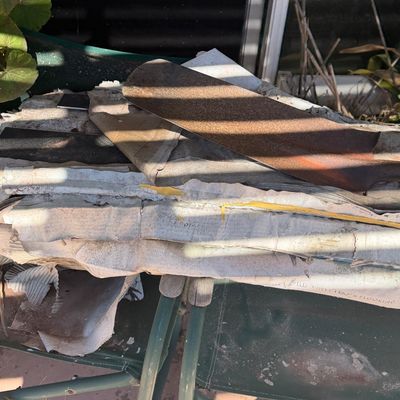 Sale Photo Thumbnail #62: Vintage rusted shovel head resting on discarded building supplies and cardboard, set atop green folding lawn chairs outdoors.