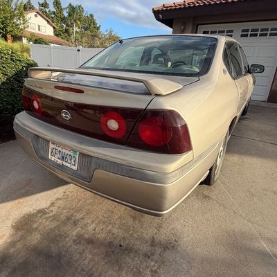 Sale Photo Thumbnail #11: Gold Chevrolet Impala LS sedan with a rear spoiler and California license plates, parked in a residential driveway.