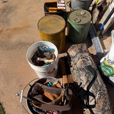 Sale Photo Thumbnail #256: Collection of outdoor and yard supplies, including buckets of hand tools, vintage metal gas and grease cans, a camouflage bag, and long-handled lawn tools.