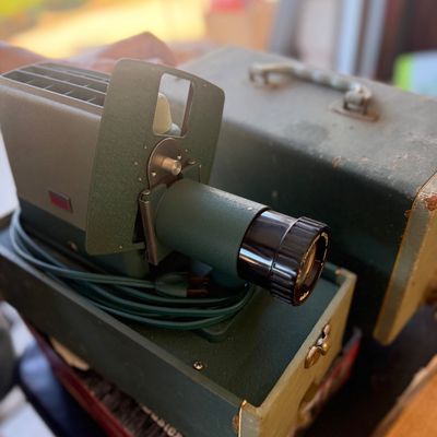 Sale Photo Thumbnail #244: Vintage mid-century olive green 35mm slide projector with attached power cord and its matching fitted carrying case.