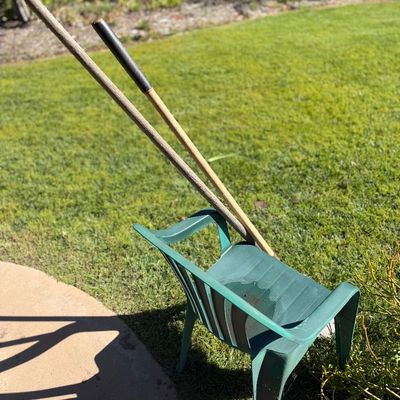 Sale Photo Thumbnail #60: A pair of long-handled wooden yard tools propped against a green plastic lawn chair outdoors.