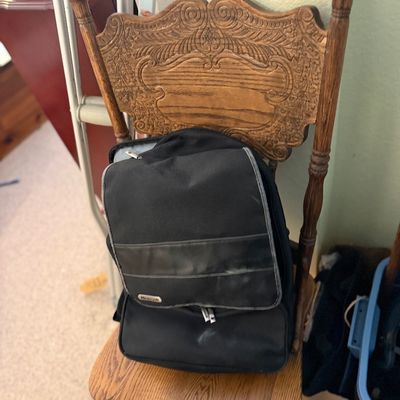 Sale Photo Thumbnail #171: Black canvas Microsoft branded backpack sitting on a vintage carved oak side chair with ornate crest detail.