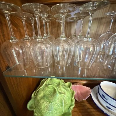 Sale Photo Thumbnail #145: Collection of clear glass stemware inverted on a glass shelf above a green cabbage-shaped ceramic covered dish and small tableware items in a wooden hutch.