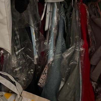 Sale Photo Thumbnail #187: Assorted clothing items hanging in a closet, many protected by plastic garment bags, alongside a yellow-and-white striped canvas tote bag.