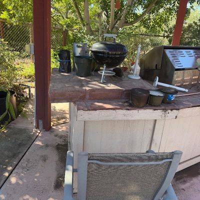 Sale Photo Thumbnail #71: Outdoor patio station featuring a small portable Weber-style kettle grill, potted plants, and an outdoor chair under a wooden pergola structure.