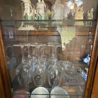 Sale Photo Thumbnail #142: Wooden display cabinet filled with glassware, Orfila-branded wine glasses, small ceramic bowls, and classical-style figurines.
