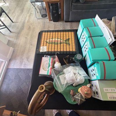 Sale Photo Thumbnail #94: Collection of tabletop decor and household goods, including a framed fish trivet, brass horn, gnome figure, and boxed items.