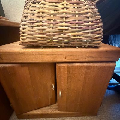 Sale Photo Thumbnail #306: Hand-woven basket with an antler handle sitting atop a small rustic wooden two-door cabinet.