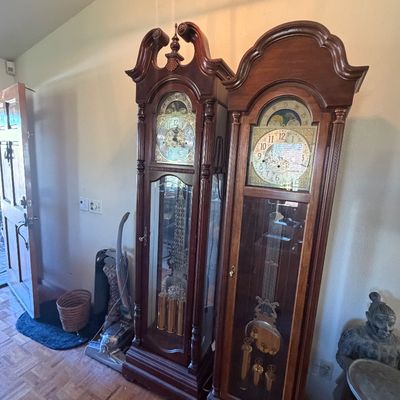 Sale Photo Thumbnail #123: Two traditional dark wood grandfather clocks featuring ornate brass dials, exposed pendulums, and decorative crest tops.