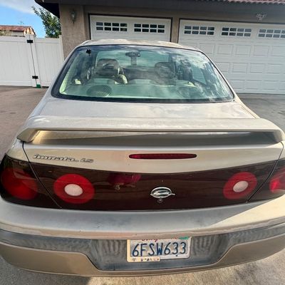 Sale Photo Thumbnail #8: Rear view of an early 2000s Chevrolet Impala LS sedan in gold paint featuring a rear spoiler and California license plate.