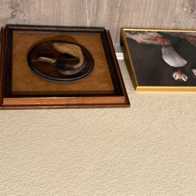 Sale Photo Thumbnail #186: Pair of framed wall art pieces, including a vintage 3D carved wood duck head emblem in a square wooden frame and a photo print of puffins in a gold-tone metal frame.