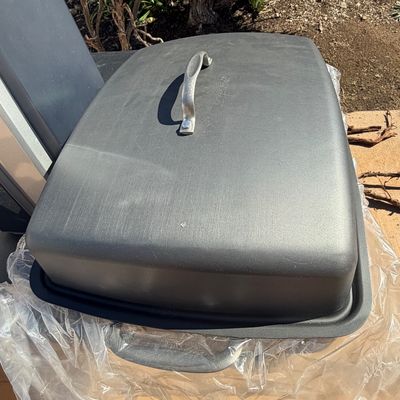 Sale Photo Thumbnail #269: Black Magnalite roasting pan with lid featuring a metal handle, shown sitting on plastic wrap outdoors.