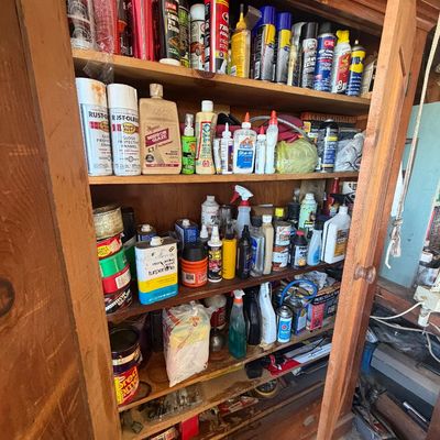 Sale Photo Thumbnail #219: Tall vintage wooden cabinet with open doors filled with assorted household cleaners, spray paints, automotive fluids, and hardware supplies.