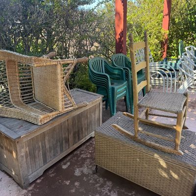 Sale Photo Thumbnail #68: Selection of outdoor patio furniture including a wooden storage chest, wicker trunk, ladder-back rocking chair, wicker armchair, and stackable green plastic lawn chairs.