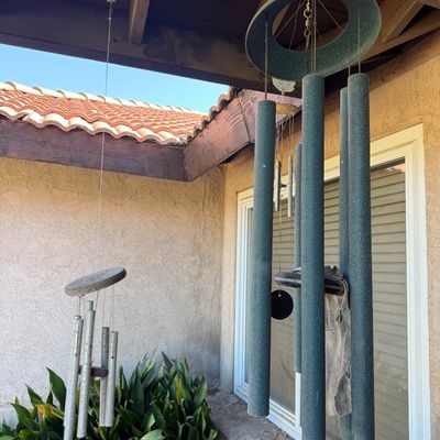 Sale Photo Thumbnail #168: Two hanging outdoor wind chimes, including a large textured green metal tubular wind chime and a smaller metallic wind chime.