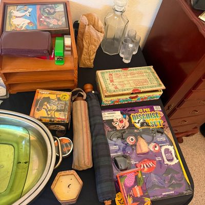 Sale Photo Thumbnail #321: Assortment of tabletop items including a novelty disguise set, a glass decanter with shot glasses, compact umbrellas, small wooden boxes, and a metal basin with a green glass insert.
