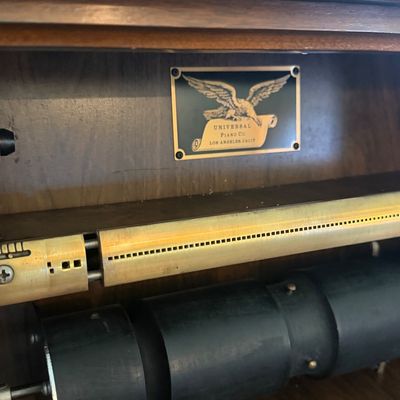 Sale Photo Thumbnail #34: Interior detail of a vintage Universal Piano Co. player piano mechanism, featuring brass tracker bar and manufacturer's eagle plaque.