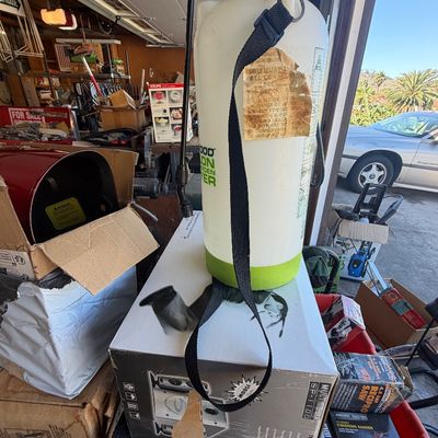Sale Photo Thumbnail #230: Used pump-style lawn and garden sprayer with shoulder strap, resting on top of boxed tools in a garage setting.