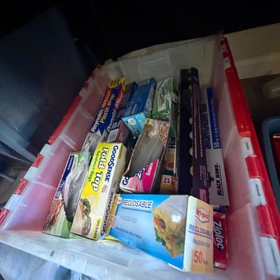 Sale Photo Thumbnail #79: Plastic storage tote filled with various household food storage supplies, including aluminum foil, plastic wrap, and sandwich bags.