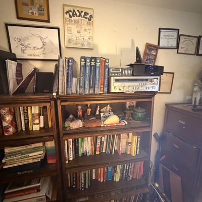 Sale Photo Thumbnail #115: Pair of vintage dark wood bookcases filled with books, small collectibles, and vintage audio equipment, alongside framed wall art.