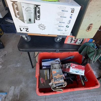 Sale Photo Thumbnail #229: A collection of boxed tools, hardware, and electronics including a Cyber Acoustics 2.1 speaker system, Chicago Electric power tools, and a vintage carrying case displayed on a folding table and in a storage bin.