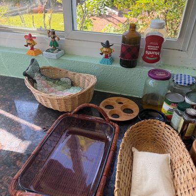 Sale Photo Thumbnail #21: Collection of kitchen items including woven baskets, a glass baking dish with a wicker holder, novelty window figurines, and pantry jars on a granite countertop.
