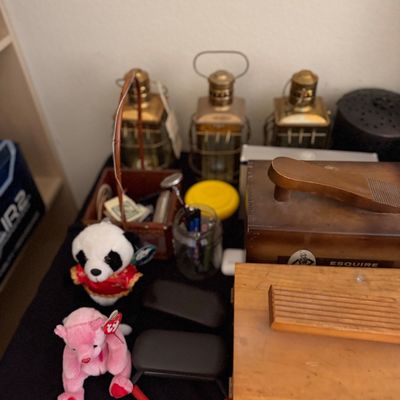 Sale Photo Thumbnail #197: Collection of tabletop decor and collectibles including an Esquire vintage shoe shine box, plush stuffed animals, brass lantern-style decanters, and wooden storage boxes.