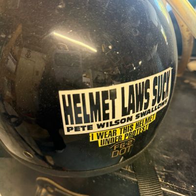 Sale Photo Thumbnail #201: Vintage black open-face motorcycle helmet adorned with novelty protest stickers referencing Pete Wilson and helmet laws.