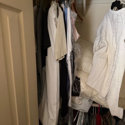 Sale Photo Thumbnail #190: Assorted men's and women's clothing, including shirts, garment bags, and a white knit sweater, hanging in a closet alongside stacked bedding.