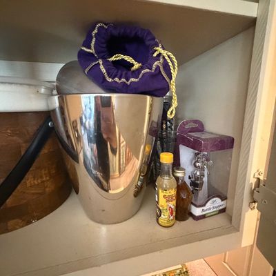 Sale Photo Thumbnail #78: Collection of barware items on a shelf, including a polished metal ice bucket, a purple velvet Crown Royal drawstring bag, mini liquor bottles, and a boxed bottle stopper.