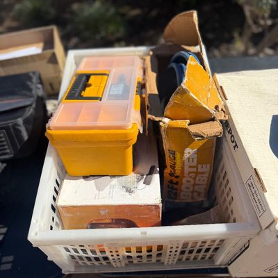 Sale Photo Thumbnail #263: Plastic crate filled with hardware supplies, including a yellow plastic toolbox organizer, boxed booster cables, and various boxed accessories.
