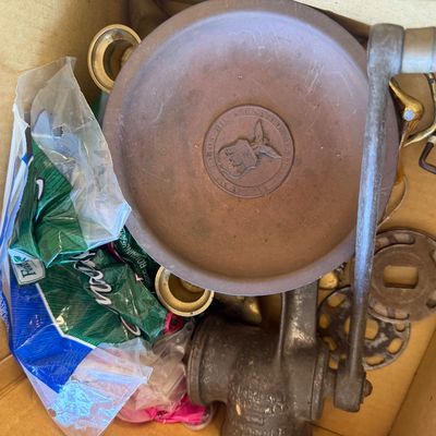 Sale Photo Thumbnail #243: Cardboard box containing a cast iron hand-crank meat grinder, brass items including an Air Force Academy dish, and various metal parts.