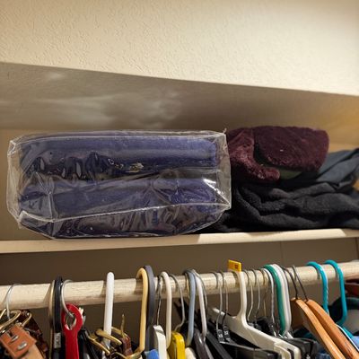 Sale Photo Thumbnail #182: Closet shelf containing a packaged blue textile, folded fleece garments, and clothes hanging on various hangers below.