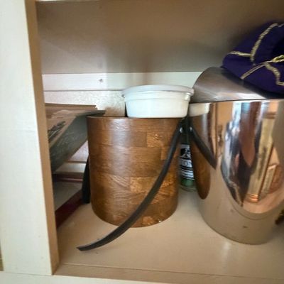 Sale Photo Thumbnail #77: Vintage mid-century wooden ice bucket with dark strap handles shown alongside a polished stainless steel ice bucket inside a shelf.