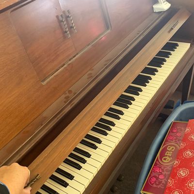 Sale Photo Thumbnail #35: Vintage mid-century wooden player piano with a sliding keyboard cover, shown alongside several Q.R.S. music roll boxes.