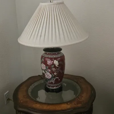 Sale Photo Thumbnail #13: Vintage Asian-style maroon porcelain ginger jar table lamp with hand-painted floral motifs and a pleated fabric shade, set on a wood and glass side table.