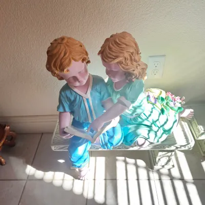Sale Photo Thumbnail #3: Painted composite resin garden statue depicting a young boy and girl sitting on a bench reading a book.