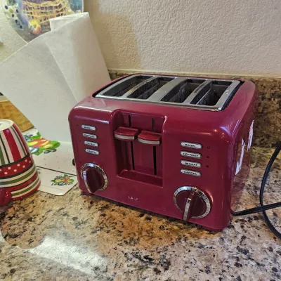 Sale Photo Thumbnail #36: Burgundy four-slot toaster sitting on a granite countertop, featuring dual control panels for bagel, defrost, reheat, and cancel settings.
