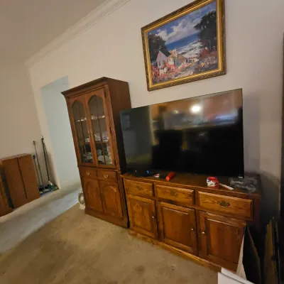 Sale Photo Thumbnail #42: A large flat-screen TV set on a traditional oak media console, positioned next to a matching oak hutch and beneath a framed landscape art print.