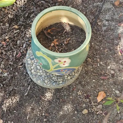 Sale Photo Thumbnail #108: Glazed ceramic outdoor planter with colorful floral motif, sitting on a pebbled concrete base.