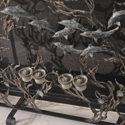 Sale Photo Thumbnail #92: Intricate metal fireplace screen featuring swimming dolphins and sea vegetation motifs, equipped with small glass votive candle holders along the base.