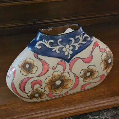 Sale Photo Thumbnail #30: Vintage flattened oval ceramic vase featuring hand-painted floral motifs and a cobalt blue neck with scrollwork.