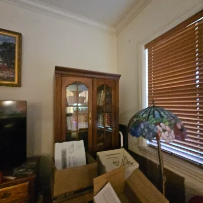 Sale Photo Thumbnail #43: A stained glass floor lamp with floral motifs sits beside a traditional wooden display cabinet filled with books.