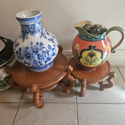 Sale Photo Thumbnail #2: Blue and white Delft-style floral ceramic vase paired with a colorful hand-painted pitcher, both displayed on carved wooden plant stands.