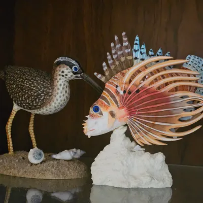 Sale Photo Thumbnail #29: Hand-painted shorebird figurine standing beside a detailed lionfish sculpture mounted on a coral-style base.