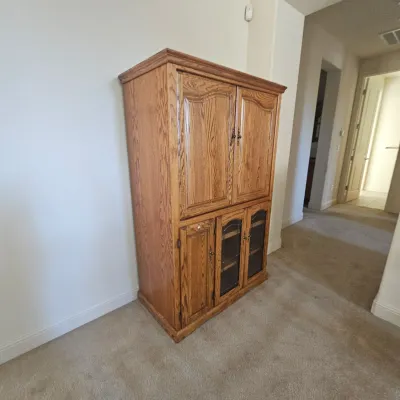 Sale Photo Thumbnail #60: Traditional golden oak entertainment armoire featuring upper double cabinet doors and lower glass-fronted storage cabinets.