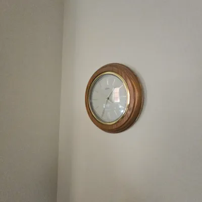 Sale Photo Thumbnail #100: Round wall clock featuring a light-toned wooden frame and a gold-tone trim surrounding a silver-white dial with Roman numerals.
