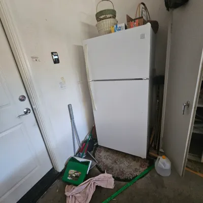 Sale Photo Thumbnail #58: White top-freezer refrigerator tucked into a utility corner alongside cleaning tools and woven baskets.